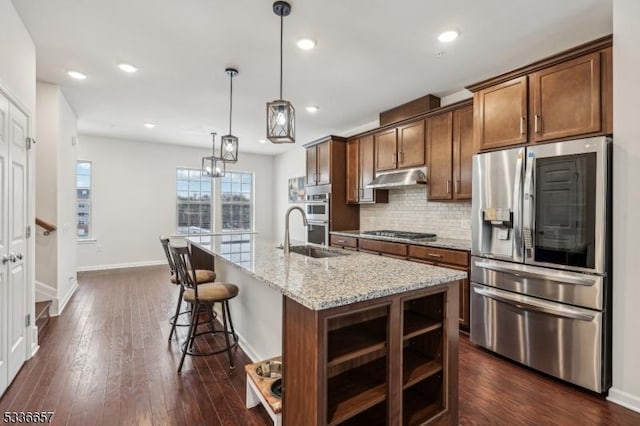 kitchen with pendant lighting, a kitchen island with sink, stainless steel appliances, light stone counters, and decorative backsplash