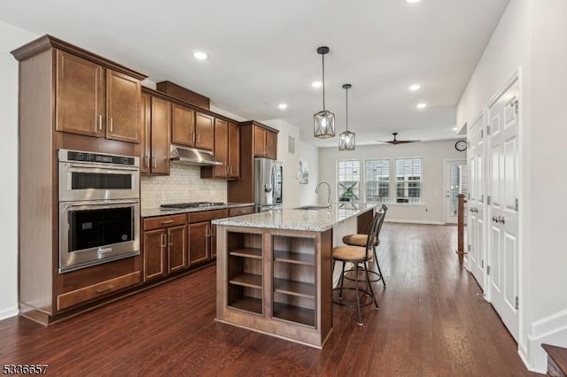 kitchen with decorative light fixtures, a breakfast bar area, light stone counters, stainless steel appliances, and a center island with sink