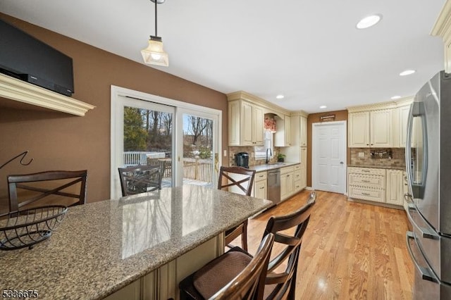 kitchen featuring hanging light fixtures, stainless steel appliances, light stone countertops, cream cabinetry, and light wood-type flooring