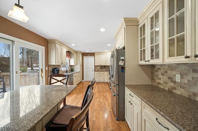 kitchen with light wood-type flooring, dark stone countertops, appliances with stainless steel finishes, pendant lighting, and cream cabinetry