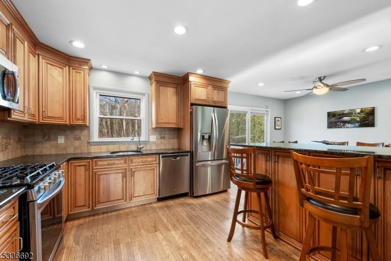 kitchen featuring sink, light hardwood / wood-style flooring, a breakfast bar area, appliances with stainless steel finishes, and tasteful backsplash