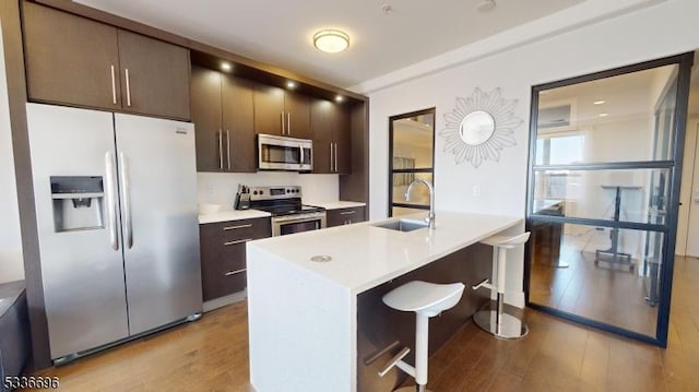 kitchen featuring appliances with stainless steel finishes, sink, a kitchen bar, dark brown cabinets, and light hardwood / wood-style flooring