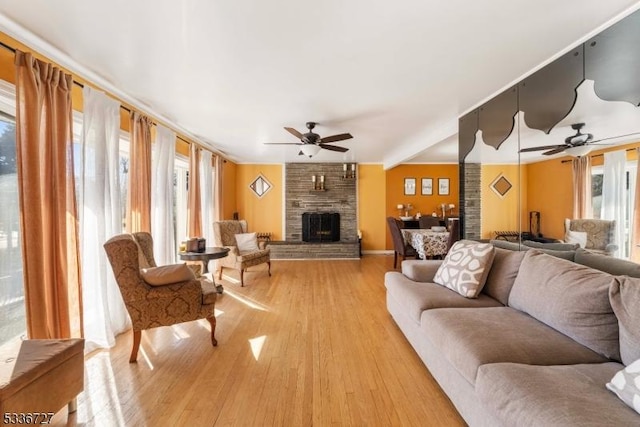 living room with light hardwood / wood-style flooring, a wealth of natural light, a large fireplace, and ceiling fan