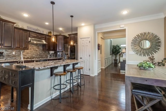 kitchen with decorative light fixtures, a kitchen breakfast bar, a kitchen island with sink, dark brown cabinetry, and stainless steel fridge with ice dispenser