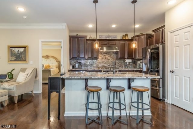 kitchen featuring pendant lighting, stainless steel refrigerator, an island with sink, a kitchen bar, and light stone countertops