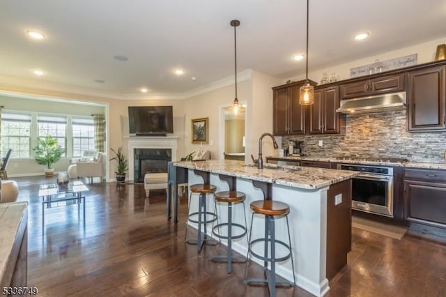 kitchen with dark brown cabinetry, sink, stainless steel oven, hanging light fixtures, and a kitchen breakfast bar