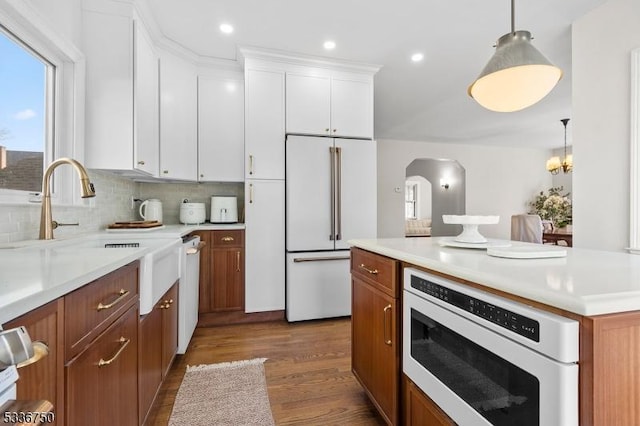 kitchen with pendant lighting, white appliances, hardwood / wood-style flooring, white cabinetry, and decorative backsplash