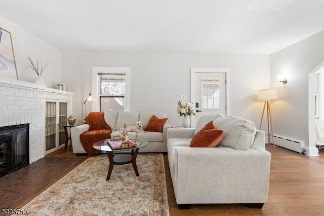 living room with dark wood-type flooring, a fireplace, and a baseboard heating unit