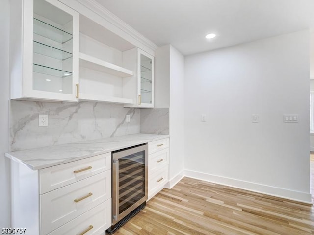 kitchen with tasteful backsplash, white cabinetry, wine cooler, light stone counters, and light hardwood / wood-style flooring