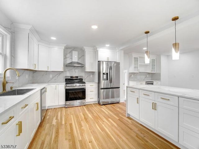 kitchen featuring wall chimney range hood, sink, white cabinets, and appliances with stainless steel finishes