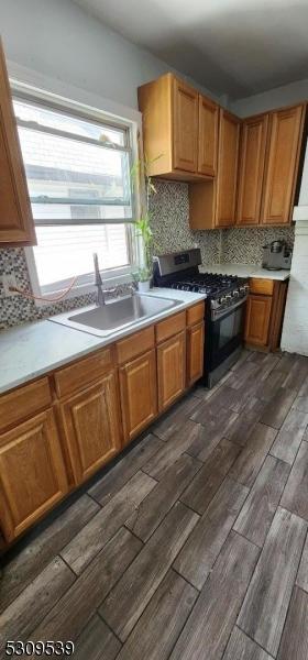 kitchen with tasteful backsplash, gas stove, sink, and dark wood-type flooring