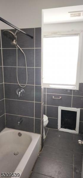 bathroom featuring tiled shower / bath combo, tile patterned flooring, and toilet