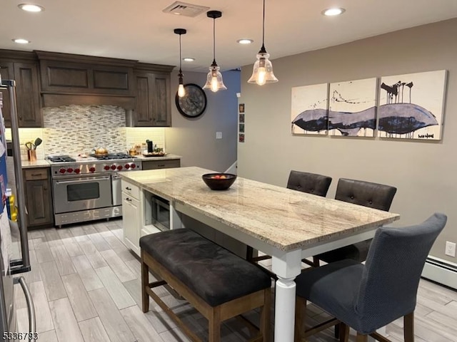 kitchen featuring dark brown cabinetry, a kitchen bar, hanging light fixtures, stainless steel appliances, and backsplash