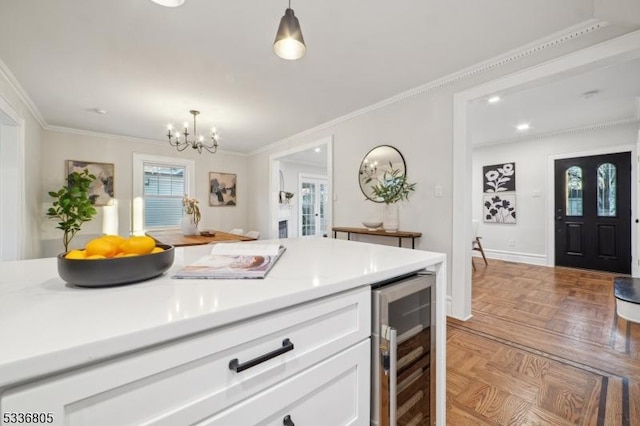 kitchen with beverage cooler, parquet floors, pendant lighting, crown molding, and white cabinets