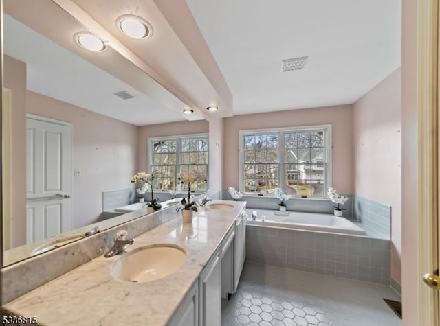 bathroom featuring a relaxing tiled tub, vanity, and tile patterned flooring