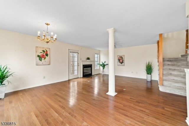 unfurnished living room with hardwood / wood-style flooring, a chandelier, and decorative columns