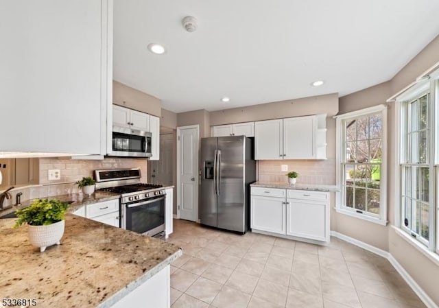 kitchen featuring light tile patterned floors, appliances with stainless steel finishes, light stone countertops, white cabinets, and decorative backsplash