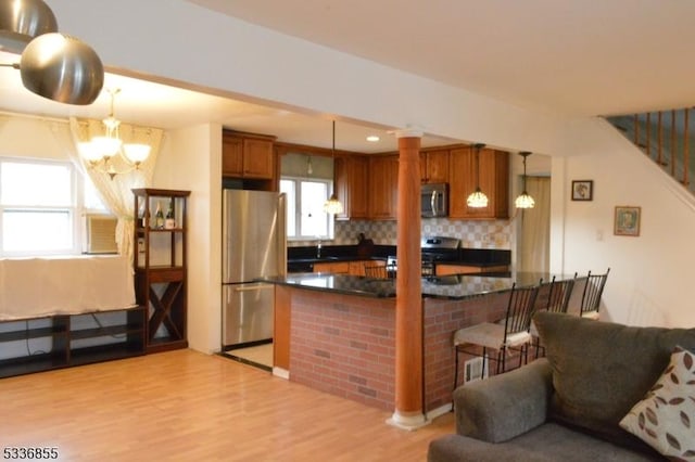 kitchen featuring appliances with stainless steel finishes, tasteful backsplash, a kitchen bar, hanging light fixtures, and light hardwood / wood-style floors