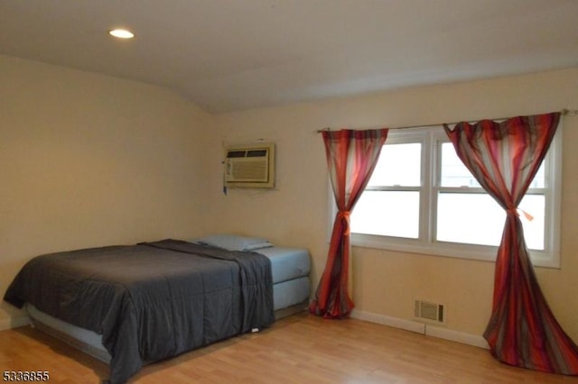 bedroom with hardwood / wood-style floors, vaulted ceiling, and an AC wall unit