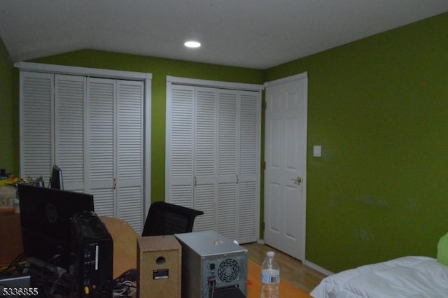 bedroom with vaulted ceiling, hardwood / wood-style floors, and two closets