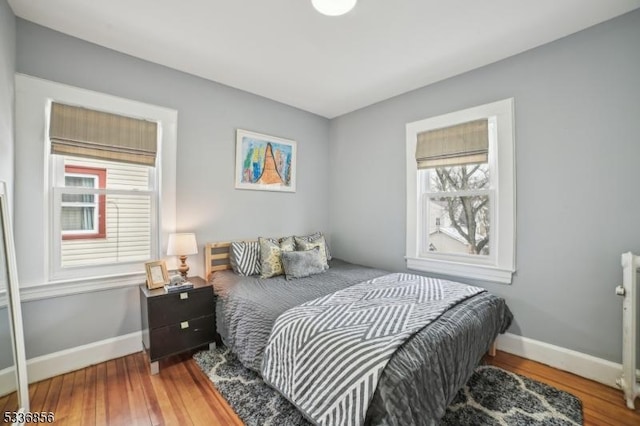 bedroom with radiator heating unit, wood finished floors, and baseboards