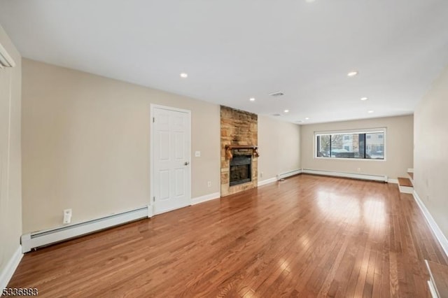 unfurnished living room featuring a baseboard radiator, a stone fireplace, and light hardwood / wood-style flooring