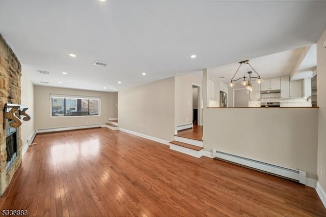 unfurnished living room with hardwood / wood-style floors, a stone fireplace, and a baseboard radiator