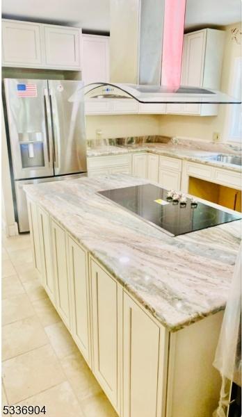 kitchen featuring stainless steel fridge, light tile patterned flooring, black electric cooktop, cream cabinetry, and wall chimney exhaust hood