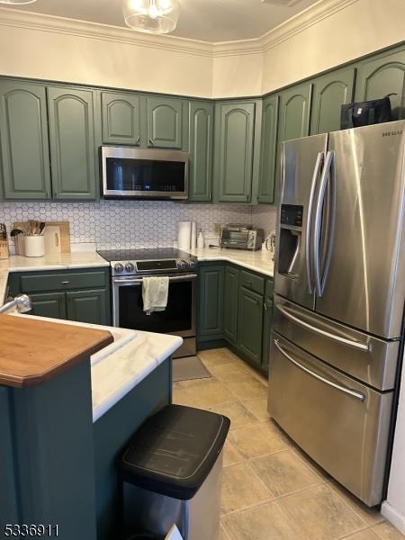 kitchen with tasteful backsplash, ornamental molding, appliances with stainless steel finishes, and green cabinets