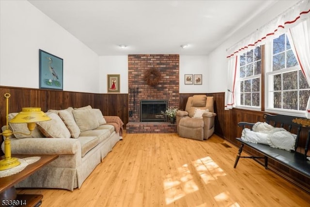 living room featuring visible vents, wooden walls, a brick fireplace, a wainscoted wall, and wood finished floors