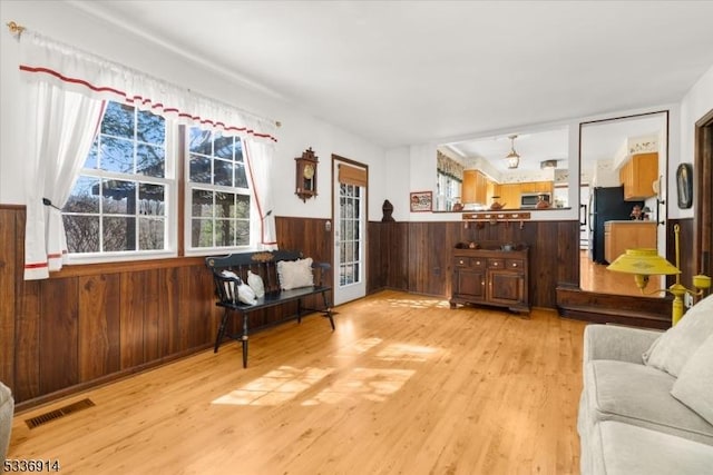 living area featuring light wood-type flooring, visible vents, wooden walls, and wainscoting