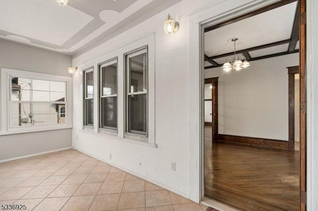 empty room featuring beam ceiling, light tile patterned floors, baseboards, and an inviting chandelier