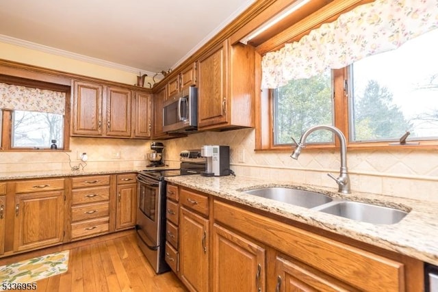 kitchen with sink, light stone counters, light hardwood / wood-style flooring, ornamental molding, and stainless steel appliances