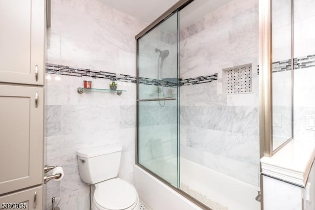 bathroom with toilet, bath / shower combo with glass door, and tile walls