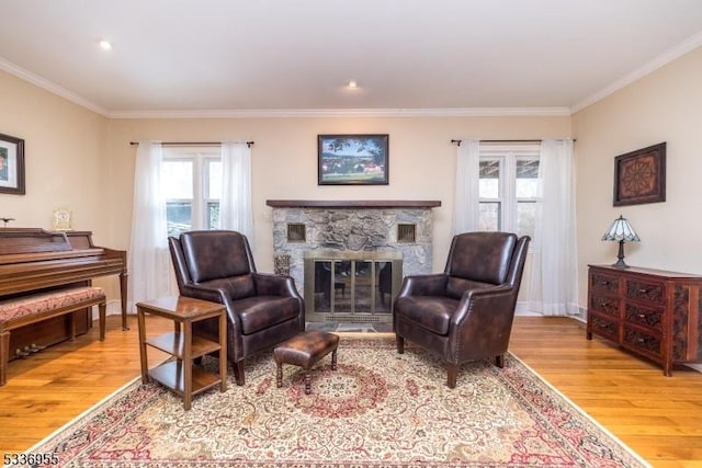 sitting room with crown molding, a stone fireplace, and light wood-type flooring