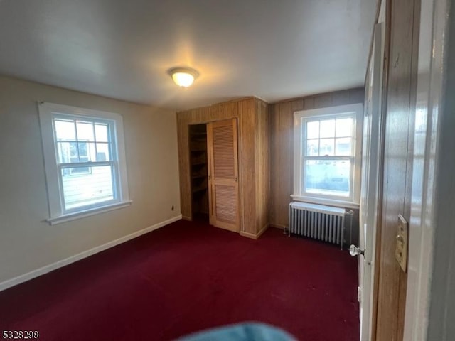 unfurnished bedroom featuring radiator, dark carpet, and a closet