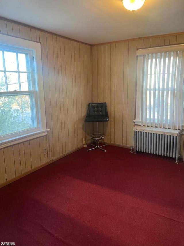 unfurnished room featuring carpet, radiator, and wood walls