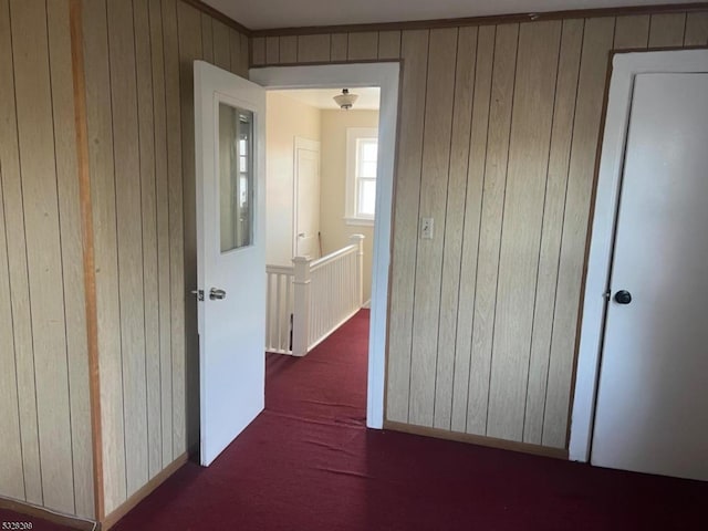 hallway featuring dark carpet and wooden walls