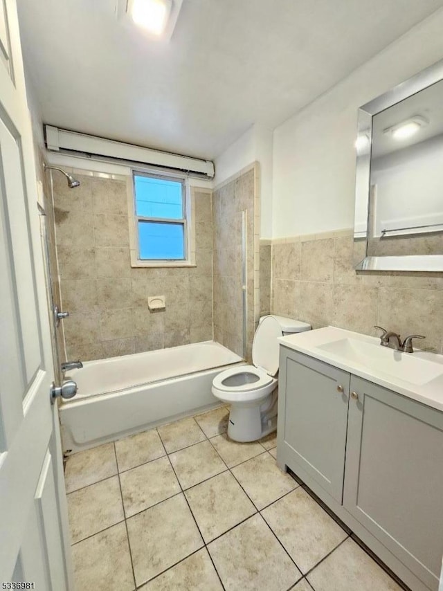 full bathroom with toilet, tile walls, vanity, tiled shower / bath combo, and tile patterned flooring