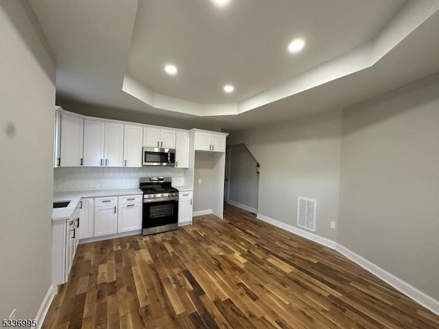 kitchen with dark wood-type flooring, white cabinetry, tasteful backsplash, appliances with stainless steel finishes, and a raised ceiling