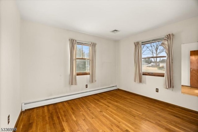 spare room featuring wood-type flooring, a baseboard radiator, and a healthy amount of sunlight