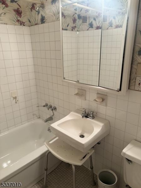 bathroom with toilet, tile patterned flooring, and tile walls