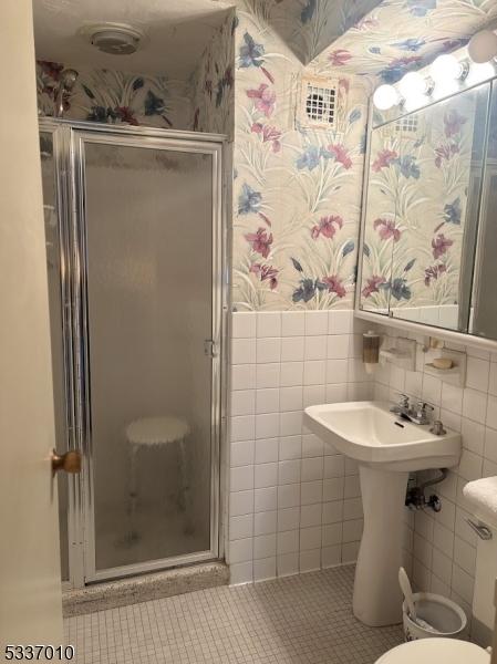 bathroom with tile walls, a shower with shower door, tile patterned floors, and toilet