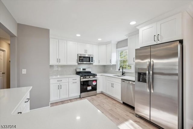 kitchen featuring appliances with stainless steel finishes, white cabinetry, sink, decorative backsplash, and light hardwood / wood-style floors