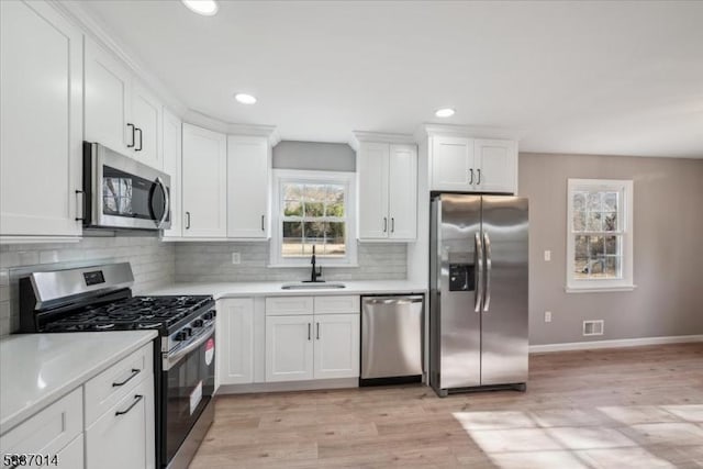 kitchen featuring stainless steel appliances, sink, white cabinets, and light wood-type flooring