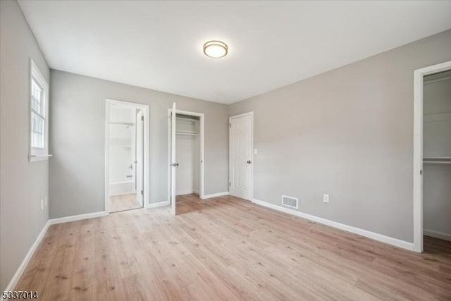 unfurnished bedroom with a walk in closet, ensuite bathroom, light hardwood / wood-style floors, and a closet