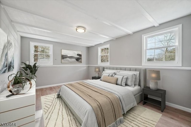 bedroom with beamed ceiling, multiple windows, and light wood-type flooring