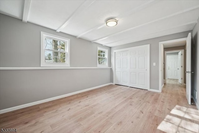 unfurnished bedroom with beamed ceiling, light hardwood / wood-style floors, and a closet