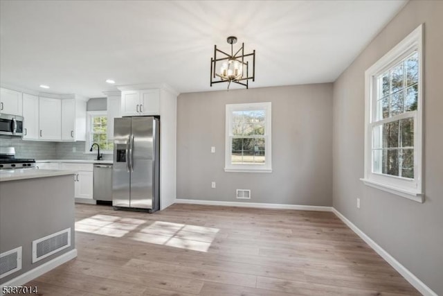 kitchen featuring white cabinetry, hanging light fixtures, stainless steel appliances, light hardwood / wood-style floors, and decorative backsplash