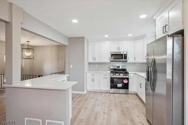 kitchen featuring white cabinetry, tasteful backsplash, hanging light fixtures, light hardwood / wood-style flooring, and appliances with stainless steel finishes